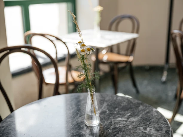 INO Café - Kavárny v Lipsku Fotografie výzdoby stolů v kavárně INO; keře ve skleněné váze; v pozadí jsou vidět další stoly v prosvětlené kavárně, gastronomie, kavárna, volný čas