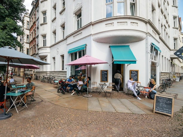 Jimmy Orpheus - Cafés in Leipzig Außenbereich des Jimmy Orpheus mit Blick auf den Eingang zum Café, farbliche Markise, Sitzbereich und den angrenzenden Straßenzug, restaurant, kulinarik