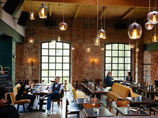 Kaiserbad - Gastronomie in Leipzig Blick in den großen Saal des Kaiserbad, mit Fokus auf den modernen Leuchten, den Backsteinwänden und den Gästen, welche ihre Mahlzeiten genießen, restaurant, kulinarik, gastronomie, freizeit
