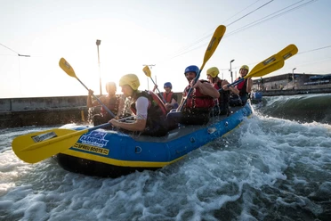 Wildwasser-Rafting im Kanupark Markkleeberg - Wassersport in Leipzig und Region Eine Gruppe sitzt mit gelben Helmen und Paddeln im Raftingboot im Kanupark Markkleeberg, Wildwasser