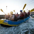 Wildwasser-Rafting im Kanupark Markkleeberg - Wassersport in Leipzig und Region Eine Gruppe sitzt mit gelben Helmen und Paddeln im Raftingboot im Kanupark Markkleeberg, Wildwasser