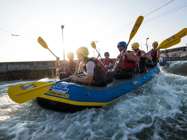 Wildwasser-Rafting im Kanupark Markkleeberg - Wassersport in Leipzig und Region Eine Gruppe sitzt mit gelben Helmen und Paddeln im Raftingboot im Kanupark Markkleeberg, Wildwasser