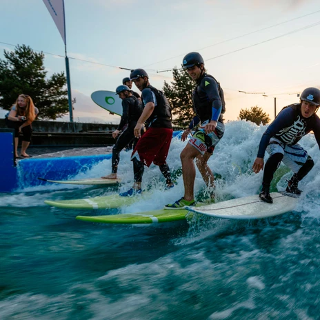Kilku mężczyzn stoi na deskach surfingowych w Markkleeberg Canoe Park i próbuje swoich sił w surfowaniu na falach