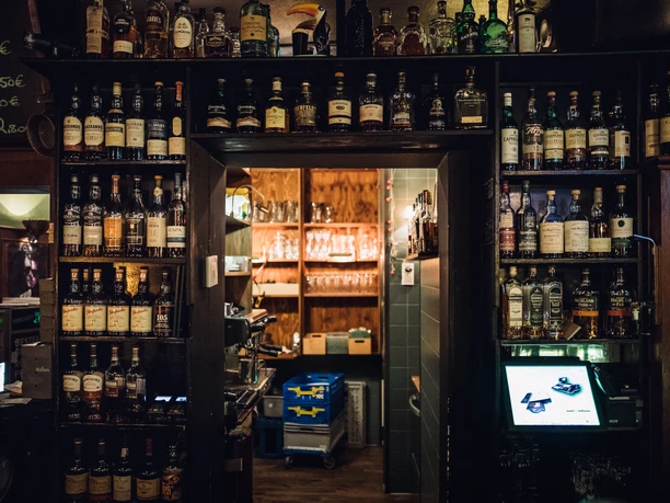 Pohled na stěnu s různými lahvemi v Killiwilly, hned vedle pokladny a s výhledem do jedné ze zadních místností, gastronomie, hospoda, bar