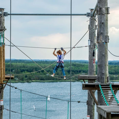 Eine Frau klettert im Kletterpark am Markkleeberger See hoch über der Erde mit Blick auf den See, Freizeitaktivität, Familienausflug