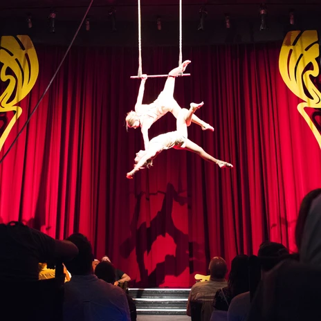 Blick durch die Zuschauerreihen auf die Bühne im Krystallpalast Varieté auf der zwei Artisten an einem Trapez hängen und performen