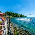 Wasserskianlage am Kulkwitzer See - Leipziger Neuseenland Eine Person fährt mit einem Wakeboard über das kristallklare Wasser des Kulkwitzer Sees, während Besucher auf einer sonnigen Terrasse entspannen.