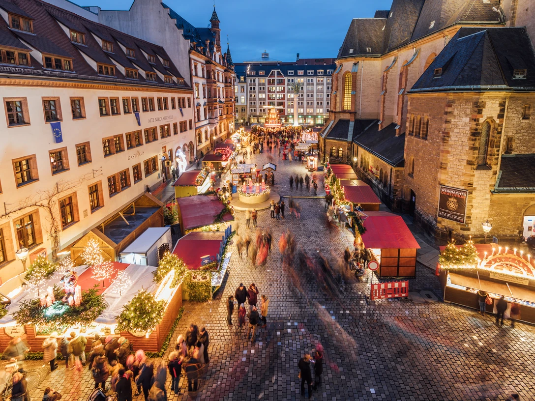 Weihnachtsmarkt auf dem Nikolaikirchhof - Weihnachten in Leipzig Blick von oben auf den Weihnachtsmarkt auf dem Nikolaikirchhof mit der Alten Nikolaischule auf der linken und der Nikolaikirche auf der rechten Seite, dazwischen Weihnachtsmarktbuden und einige Besucher zur Abenddämmerung