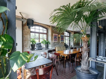 Moertelwerk - Gastronomie in Leipzig Fotografie des Innenraums des Restaurants, mit dunklem Holzmobiliar, der Bar im Hintergrund, Beleuchtung und Blick auf die großen Fenster, die helles Licht in den Saal fallen lassen, gastronomie, restaurant, bar, freizeit