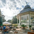 Musikpavillon - Gastronomie in Leipzig Fotografie des Freisitzes und schönen weißen Pavillons an einem Sommertag im Clara-Zetkin-Park; mit Bewaldung im Hintergrund, Sonnenschirmen