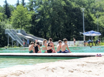 NaturSportBad Bad Düben - Piscines en plein air dans la région de Leipzig Six enfants assis au bord du bassin, dos à la caméra, en maillot de bain, laissant leurs jambes se balancer dans l'eau, avec un grand toboggan en arrière-plan, loisirs, amusement