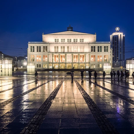 Blick auf die beleuchtete Oper Leipzig mit Spiegelungen der Lichter auf dem nassen Boden des Augustusplatz die eine wahre Sehenswürdigkeit der Musikstadt Leipzig ist, Kultureinrichtung, Veranstaltungen