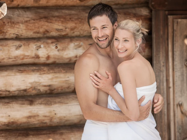 A happy couple arm in arm with towels in front of the earth sauna in the Sachsen-Therme Leipzig.