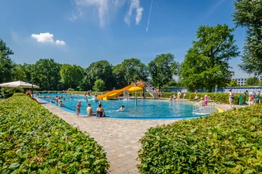 Schreberbad Leipzig - Freizeiterlebnisse in der Leipzig Region Blick auf das Hauptschwimmbecken im Schreberbad, mit gelber Rutsche und vielen Badegästen an einem Sommertag, Freizeitaktivität, Badespaß