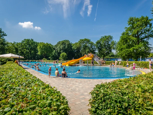 Schreberbad Leipzig - Freizeiterlebnisse in der Leipzig Region Blick auf das Hauptschwimmbecken im Schreberbad, mit gelber Rutsche und vielen Badegästen an einem Sommertag, Freizeitaktivität, Badespaß