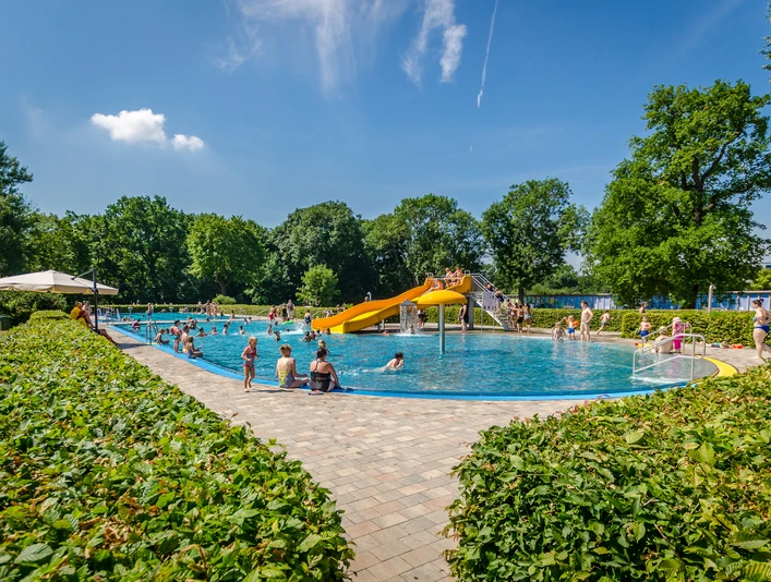 Schreberbad Leipzig - Freizeiterlebnisse in der Leipzig Region Blick auf das Hauptschwimmbecken im Schreberbad, mit gelber Rutsche und vielen Badegästen an einem Sommertag, Freizeitaktivität, Badespaß