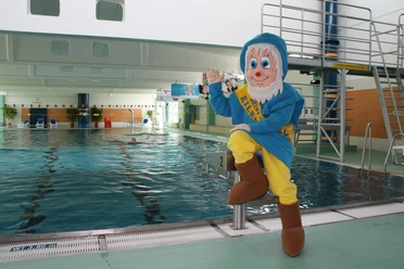 La piscine de la Schwimmhalle Eilenburg, la mascotte en costume de nain est assise sur un des plots de départ et fait signe, Piscines, Actif, Loisirs