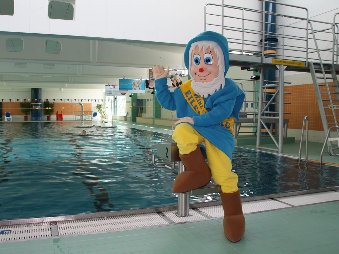 Schwimmhalle Eilenburg - Schwimmbäder in der Leipzig Region Das Schwimmbecken der Schwimmhalle Eilenburg, das Maskottchen im Zwerg-Kostüm sitzt auf einem der Startblöcke und winkt, Schwimmbäder, Aktiv, Freizeit