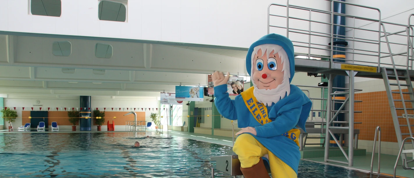 Schwimmhalle Eilenburg - Schwimmbäder in der Leipzig Region Das Schwimmbecken der Schwimmhalle Eilenburg, das Maskottchen im Zwerg-Kostüm sitzt auf einem der Startblöcke und winkt, Schwimmbäder, Aktiv, Freizeit