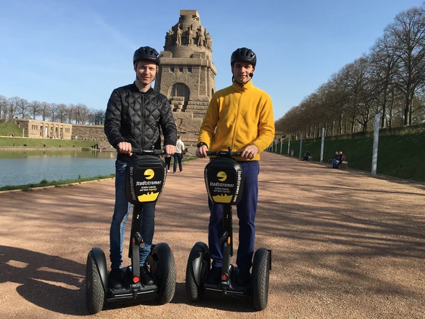 Stadtstromer Segwaytour - Erlebnisanbieter in Leipzig Blick auf das Völkerschlachtdenkmal Leipzig im Hintergrund und zwei Männer auf Segways die eine Stadtführung des Erlebnisanbieters Stadtstromer besuchen