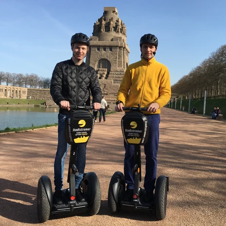Stadtstromer Segwaytour - Fournisseurs d'expériences à Leipzig Vue sur le monument de la bataille des nations à Leipzig en arrière-plan et deux hommes sur des Segways qui participent à une visite guidée de la ville organisée par le fournisseur d'expériences Stadtstromer.