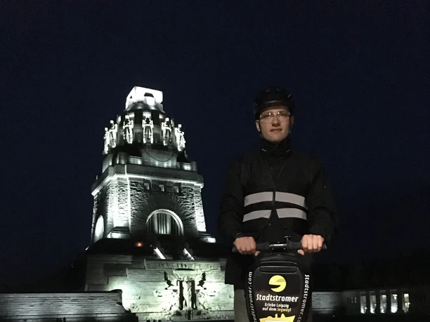 Stadtstromer Segwaytour - Erlebnisanbieter in Leipzig Blick auf das Völkerschlachtdenkmal Leipzig bei Nacht im Hintergrund und einen Mann auf Segway der eine Stadtführung des Erlebnisanbieters Stadtstromer besucht