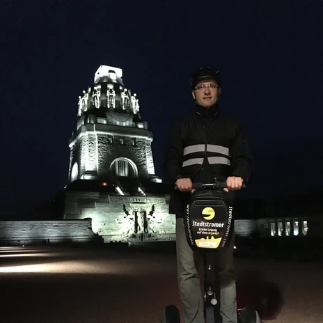Stadtstromer Segwaytour - Experience providers in Leipzig View of the Völkerschlachtdenkmal Leipzig at night in the background and a man on a Segway visiting a city tour of the experience provider Stadtstromer