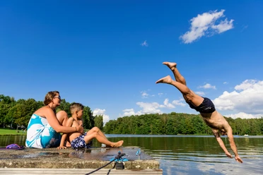 Baden im Thümmlitzsee bei Grimma Ein Mann springt kopfüber in den idyllischen Thümmlitzsee; am Ufer beobachten eine Frau und ein Kind.