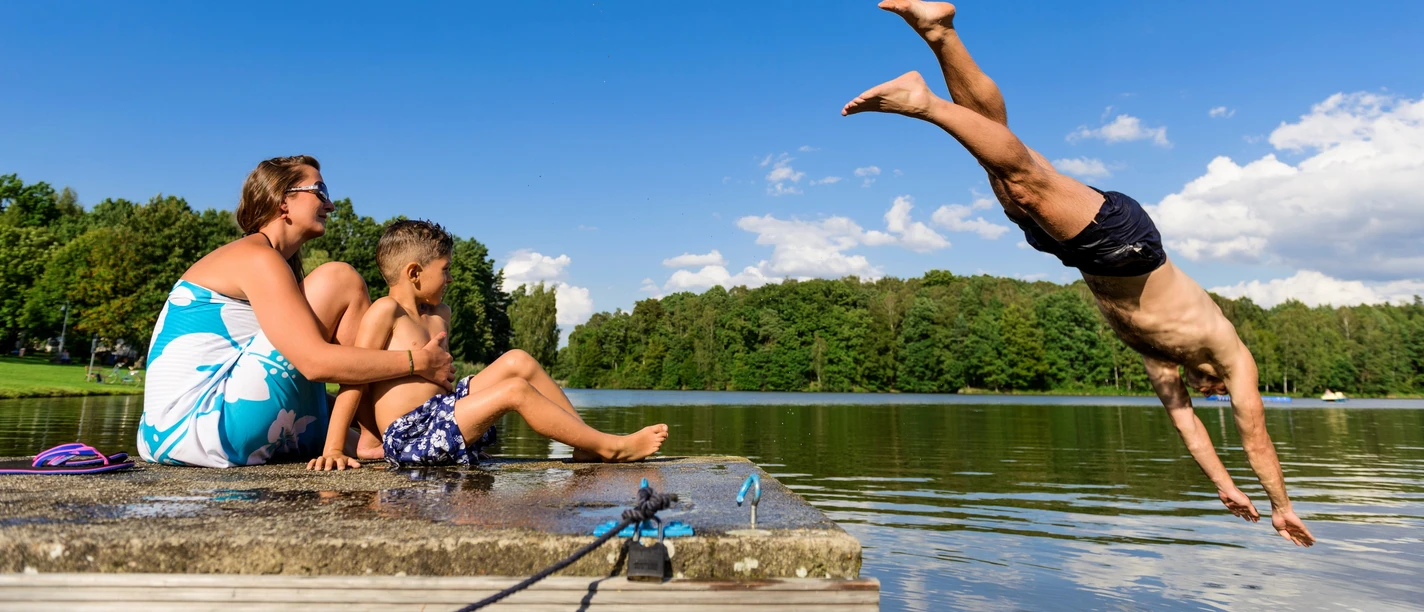 Baden im Thümmlitzsee bei Grimma Ein Mann springt kopfüber in den idyllischen Thümmlitzsee; am Ufer beobachten eine Frau und ein Kind.