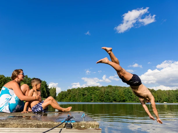 Baignade dans le lac de Thümmlitz près de Grimma Un homme plonge la tête la première dans l'idyllique lac de Thümmlitz ; sur la rive, une femme et un enfant observent.