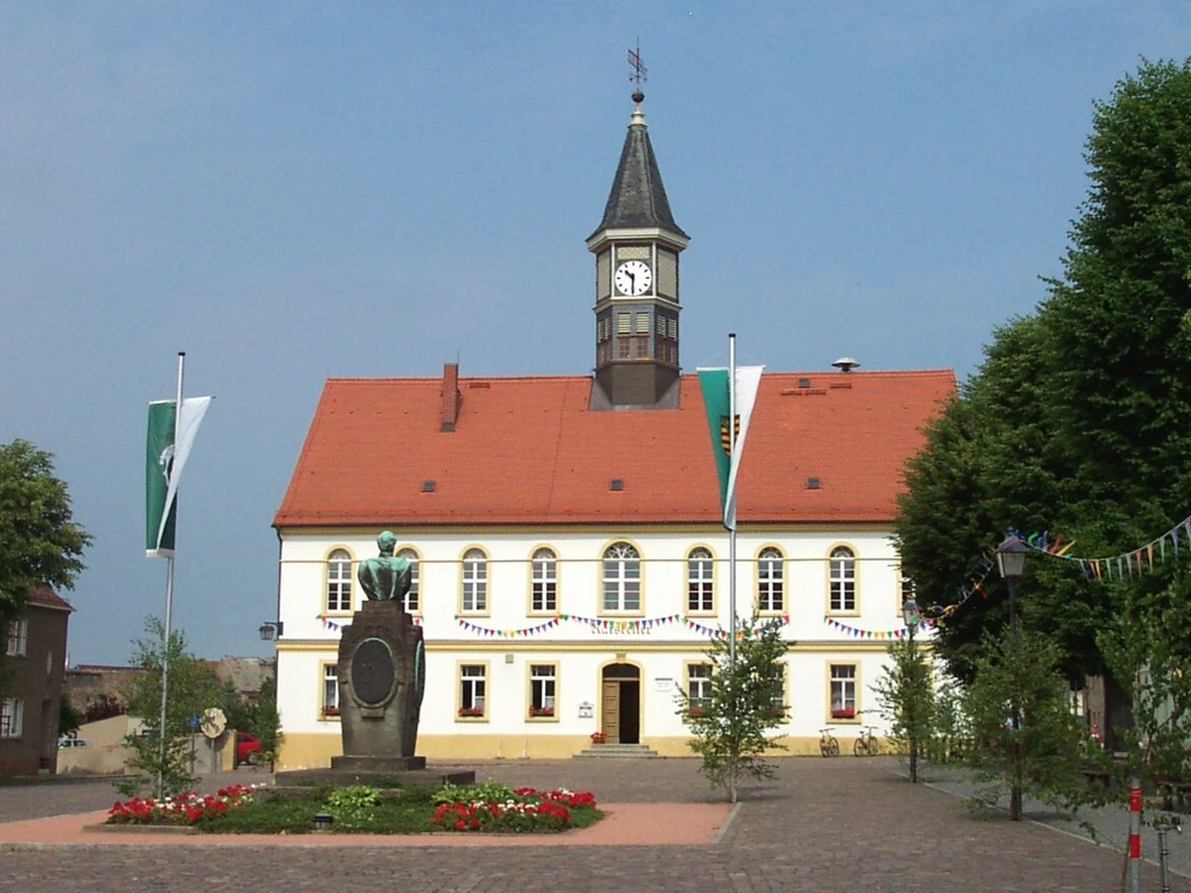 Rathaus Am Marktplatz Schildau Das Bild zeigt das Rathaus von Schildau mit Turmuhr und dem Brunnen auf dem Marktplatz.