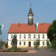 Rathaus Am Marktplatz Schildau Das Bild zeigt das Rathaus von Schildau mit Turmuhr und dem Brunnen auf dem Marktplatz.