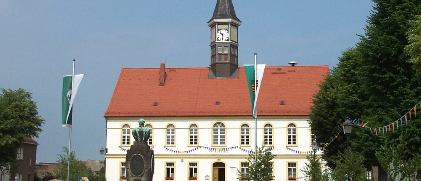 Rathaus Am Marktplatz Schildau Das Bild zeigt das Rathaus von Schildau mit Turmuhr und dem Brunnen auf dem Marktplatz.