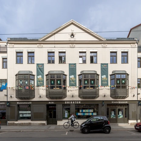 Widok z zewnątrz na muzeum dla dzieci Unikatum, napis "UNIKATUM" wielkimi literami w oknach, duże plakaty i kolorowa girlanda wiszą na fasadzie, rodzina, instytucja kultury, obiekt rekreacyjny