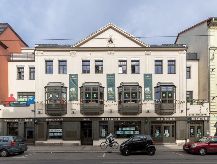 UNIKATUM Kindermuseum mit Museumscafé Goetz - Museen in Leipzig Außenansicht des Unikatum Kindermuseum, in den Fenstern klebt u.a. in Großbuchstaben "UNIKATUM", an der Fassade hängen große Plakate und eine bunte Girlande, Familie, Kultureinrichtung, Freizeiteinrichtung