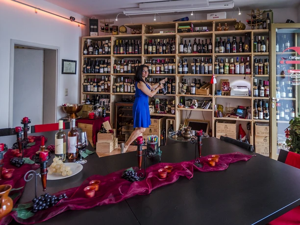 View into the wine and events bar and the huge wall shelf with wine bottles, with saleswoman, decoration, laid table in the foreground, vinothek, weinbar