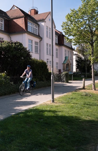Radfahrer auf einem sonnigen Weg entlang des Friedrichstaler Kanals in Detmold, gesäumt von Häusern.