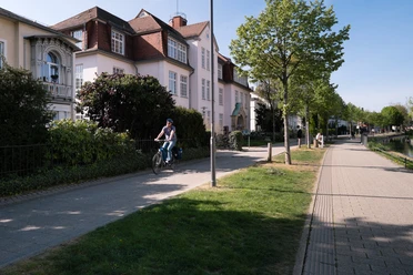 Friedrichstaler Kanal Detmold Radfahrer auf einem sonnigen Weg entlang des Friedrichstaler Kanals in Detmold, gesäumt von Häusern.