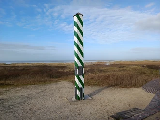 Nordwestlichster Punkt Deutschlands Eine grün-weiß gestreifte Säule steht auf einer sandigen Küstendüne, im Hintergrund die Nordsee.