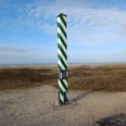 Nordwestlichster Punkt Deutschlands Eine grün-weiß gestreifte Säule steht auf einer sandigen Küstendüne, im Hintergrund die Nordsee.