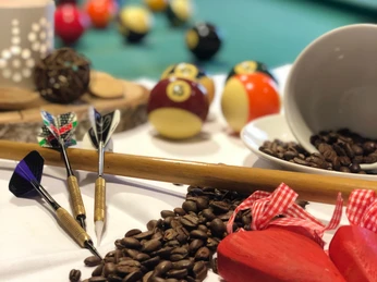 KIZ Café SoLero Bad Oeynhausen 2.jpg Auf dem Bild sind Billiardkugeln zu sehen, daneben liegen Dartscheiben, die an einem Billardstock angelehnt sind, sowie Kaffeebohnen.