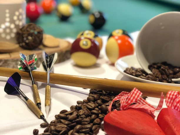 KIZ Café SoLero Bad Oeynhausen 2.jpg Auf dem Bild sind Billiardkugeln zu sehen, daneben liegen Dartscheiben, die an einem Billardstock angelehnt sind, sowie Kaffeebohnen.
