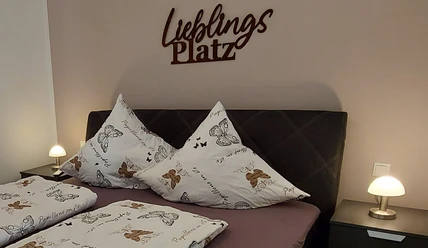 moderne_ferienwohnung_lieblingsplatz2.jpg Ein stilvoll eingerichtetes Schlafzimmer mit einem Doppelbett, dekorativen Schmetterlingskissen und sanfter Beleuchtung.