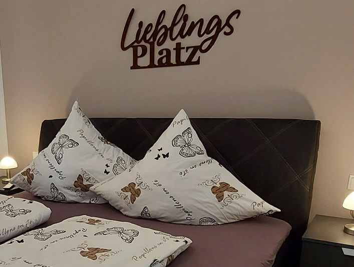 moderne_ferienwohnung_lieblingsplatz2.jpg Ein stilvoll eingerichtetes Schlafzimmer mit einem Doppelbett, dekorativen Schmetterlingskissen und sanfter Beleuchtung.