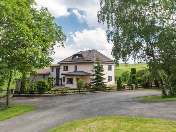 Das Foto zeigt die Außenansicht des Hauses, umgeben von einem Zaun und viel Grün.