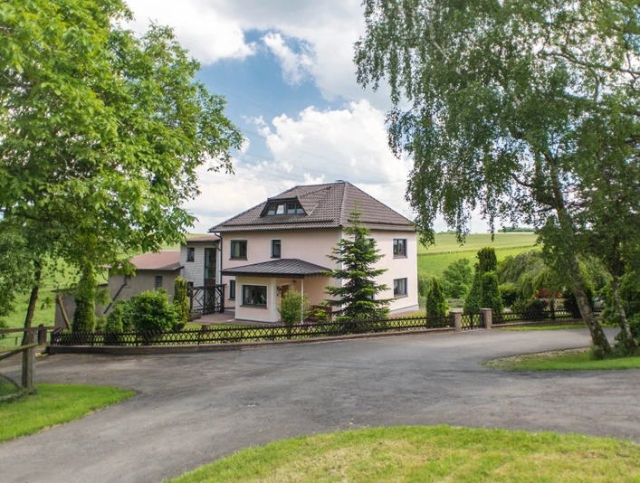 Das Foto zeigt die Außenansicht des Hauses, umgeben von einem Zaun und viel Grün.