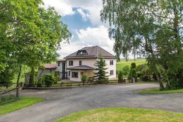 Hausansicht Das Foto zeigt die Außenansicht des Hauses, umgeben von einem Zaun und viel Grün.