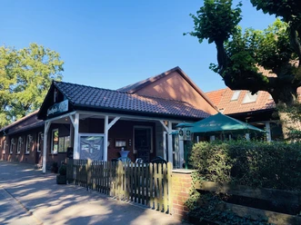 Restaurant front with red bricks, white wooden strips and a garden with parasol.