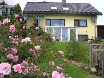 Blick aus dem Garten: Hausansicht mit Wintergarten, gepflegtem Garten und Rosenbüschen im Vordergrund.