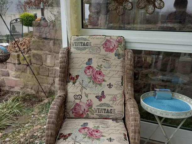 Terrasse Rattanstuhl mit floralem Polster neben rundem Bistrotisch auf einer ruhigen Terrasse.